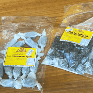 uas embalagens de balas de banana sobre superfície de madeira: à esquerda a versão Zero Açúcar (150g) e à direita a Caseira de Morretes (200g), ambas com rótulo amarelo.