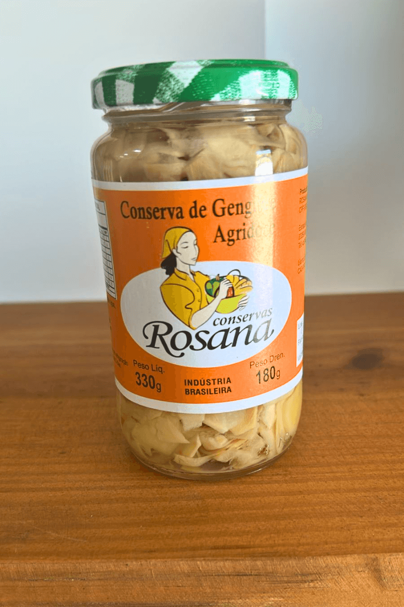 "Pote de vidro de Conserva de Gengibre Agridoce Rosana de 330g com tampa xadrez verde, mostrando as lâminas claras de gengibre em conserva.