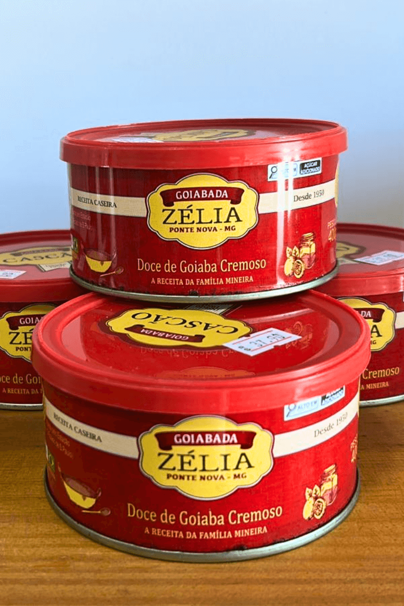 Empilhamento de latas vermelhas de Goiabada Zélia de Ponte Nova - MG, destacando o rótulo "Doce de Goiaba Cremoso" e a tradição desde 1950.