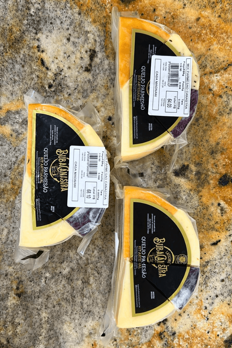 Três unidades do Kit Artesanal Queijo Parmesão BubaCanastra mostrando as fatias de parmesão tradicional, defumado, condimentado e ao vinho embaladas a vácuo.