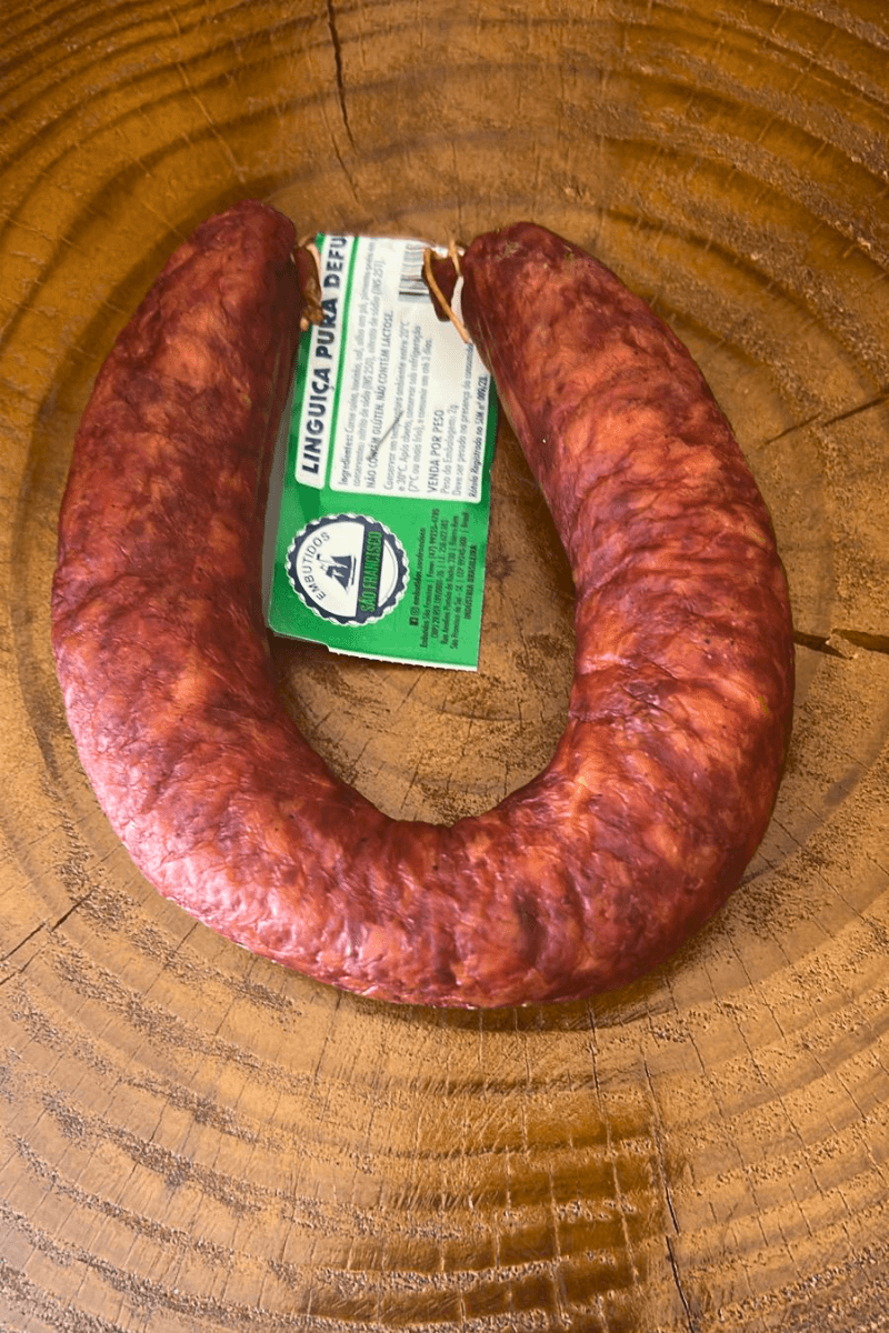 Linguiça Pura Defumada da Embutidos São Francisco em formato de ferradura sobre uma superfície de madeira rústica, destacando a etiqueta verde e branca.