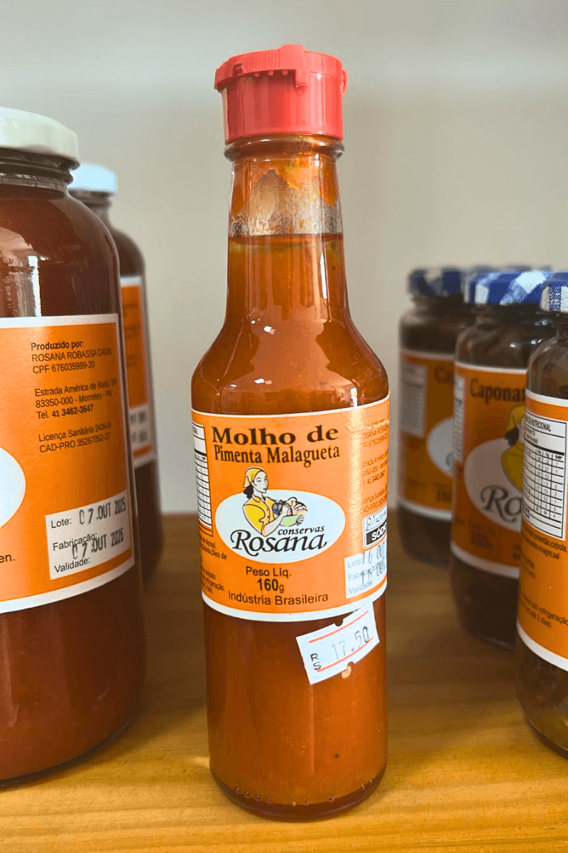 Frasco de plástico transparente com bico dosador vermelho, contendo Molho de Pimenta Malagueta Rosana de 160g, destacando a cor laranja vibrante.