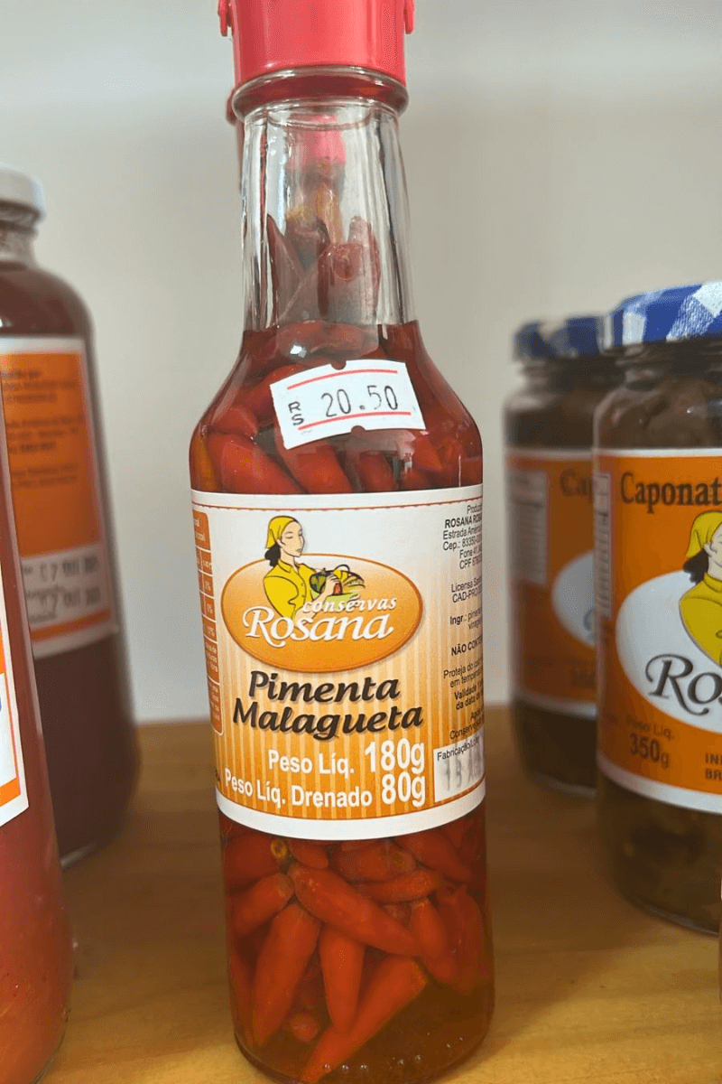 "Frasco de vidro alto de Pimenta Malagueta Rosana de 180g, com tampa vermelha, mostrando as pimentas inteiras e avermelhadas em conserva.