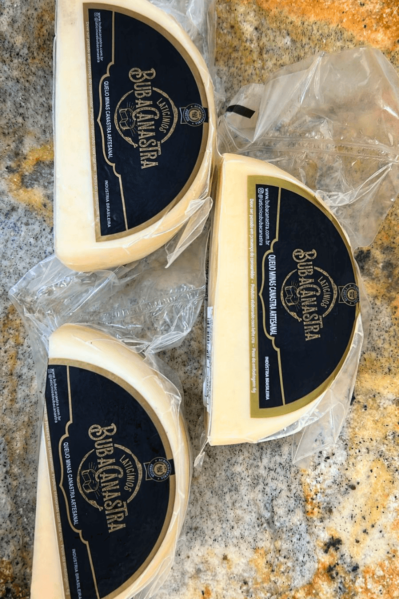 Três pedaços de Queijo Minas Canastra Artesanal em formato de meia-lua, embalados a vácuo com rótulo azul e dourado da Laticínios Buba Canastra.