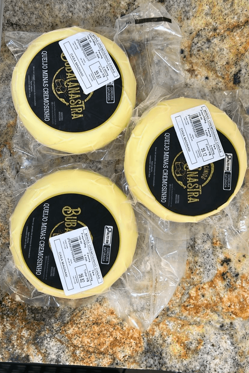 Três unidades de Queijo Minas Cremosinho Canastra embaladas a vácuo sobre bancada de granito, exibindo rótulo preto com informações nutricionais.