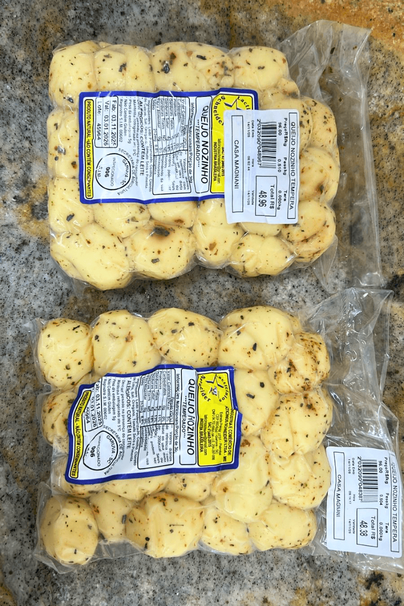 Duas embalagens de Queijo Nozinho Temperado da Laticínios Schneider sobre superfície de granito, mostrando os nozinhos com orégano e ervas.
