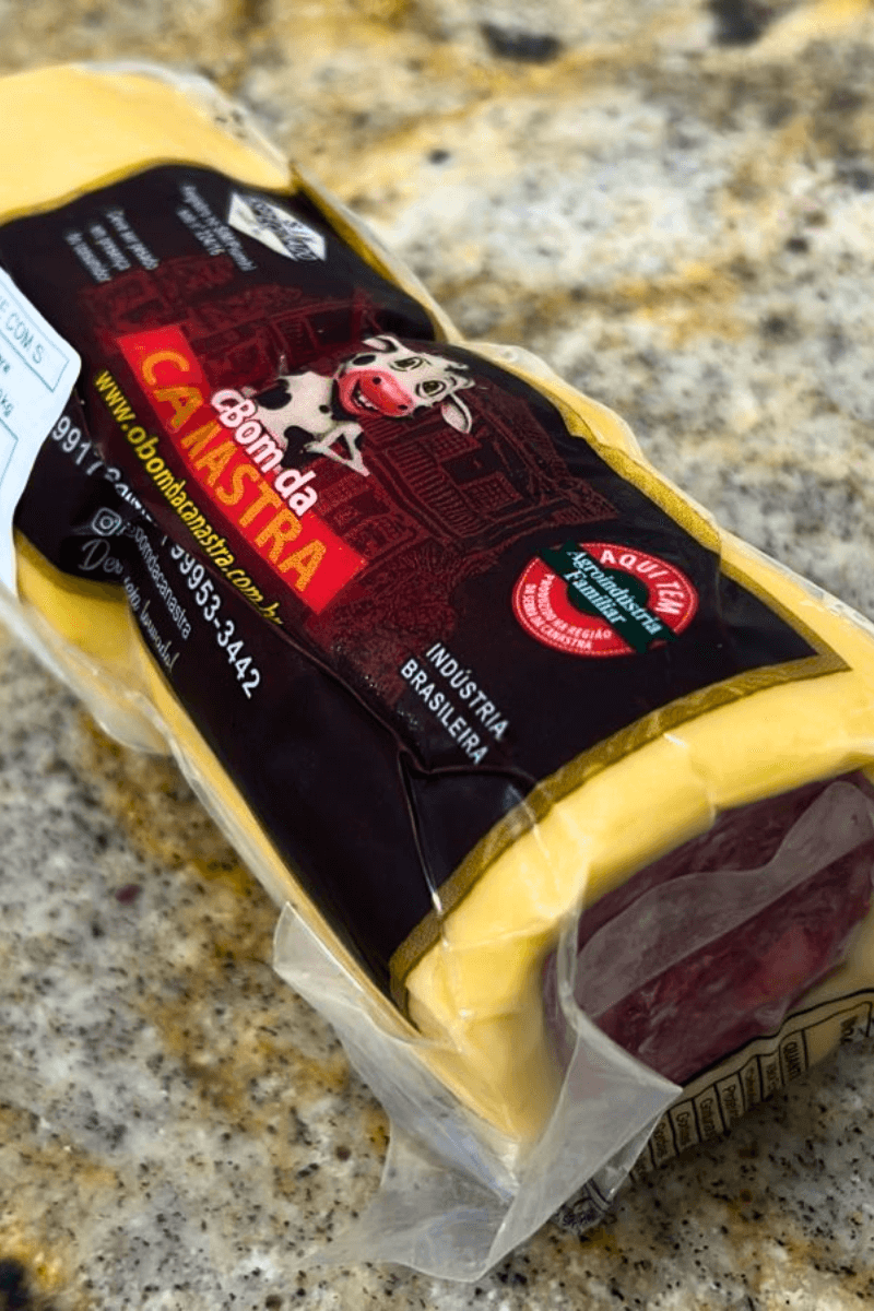 Peça de Queijo Provolone recheado com salame da marca Bom da Canastra em embalagem a vácuo, destacando o rótulo preto e vermelho com a ilustração de uma vaca sorridente.