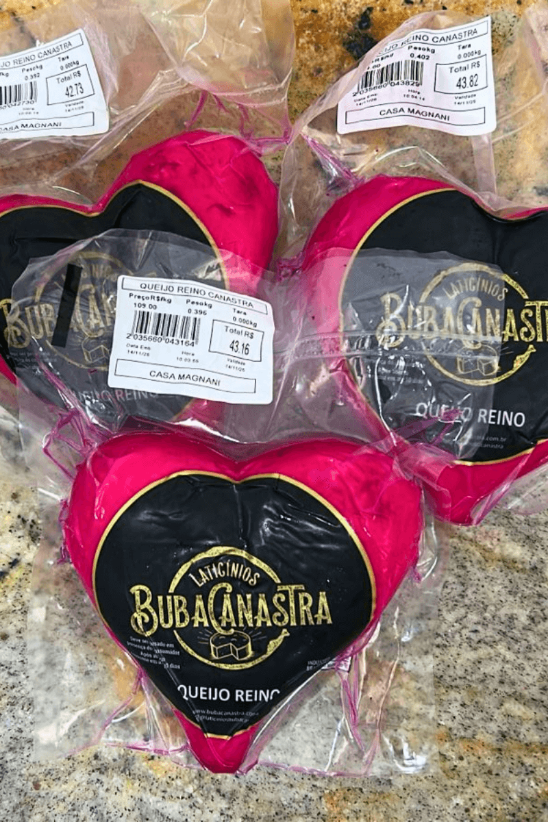 Três unidades de Queijo Reino Canastra BubaCanastra em formato de coração, com casca magenta e embaladas a vácuo sobre bancada de granito.
