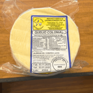 Queijo Colonial artesanal da Laticínios Schneider, peça inteira embalada a vácuo sobre superfície de madeira, evidenciando a textura clara e o selo de inspeção.