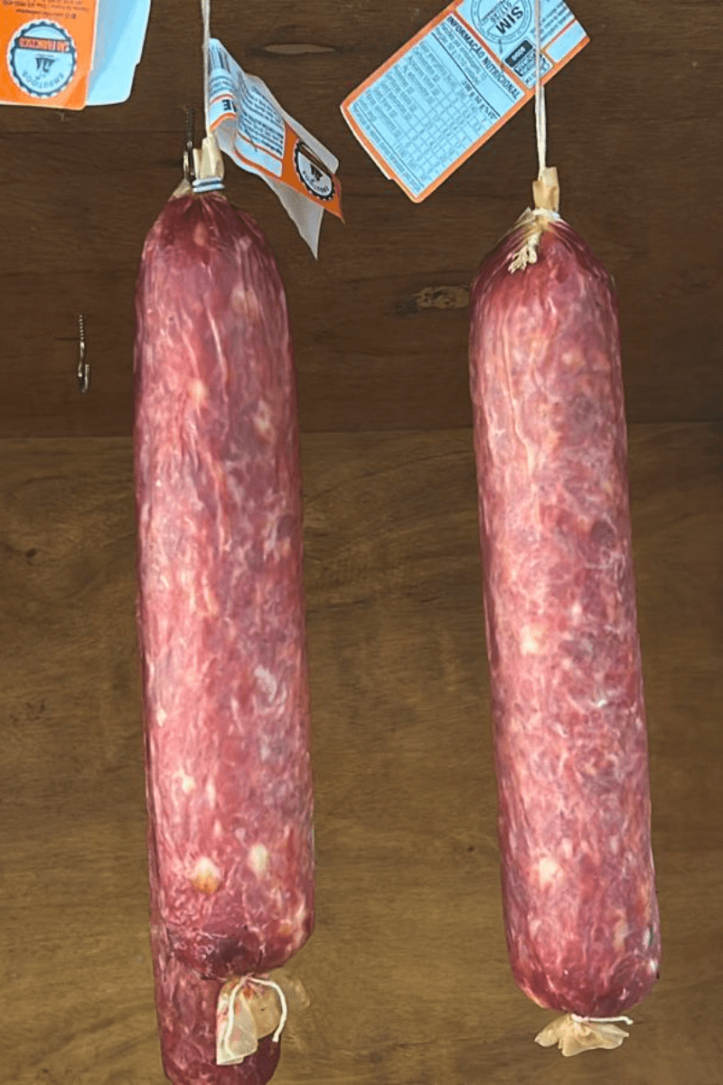 Duas peças de Salame Colonial artesanal da Embutidos São Francisco penduradas, exibindo a textura da cura e etiquetas de inspeção S.I.M.