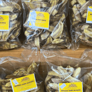 Vários pacotes de Banana Chips Sítio do Campo expostos em uma prateleira, mostrando as versões Doce e Salgada com rótulos amarelos.