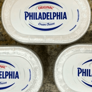 Três embalagens ovais brancas de Cream Cheese Philadelphia Original, com o logotipo azul em destaque e a frase "O 1º Cream Cheese do Mundo".