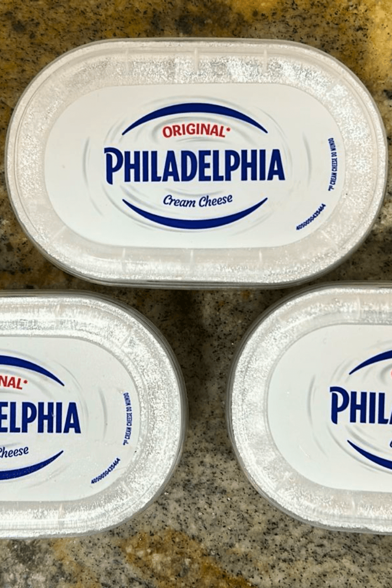Três embalagens ovais brancas de Cream Cheese Philadelphia Original, com o logotipo azul em destaque e a frase "O 1º Cream Cheese do Mundo".