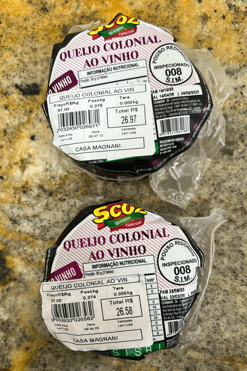 Duas peças fracionadas de Queijo Colonial ao Vinho da marca Scoz, embaladas a vácuo, com casca de tonalidade arroxeada e rótulo destacando o selo de inspeção S.I.M. 008 de Pouso Redondo.