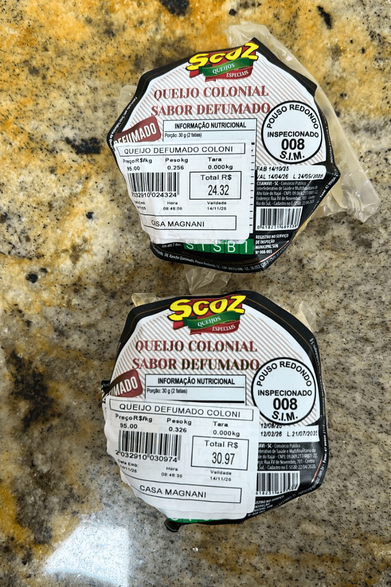 Peças fracionadas de Queijo Colonial Sabor Defumado da marca Scoz, embaladas a vácuo, com casca levemente dourada e rótulo destacando o selo de inspeção S.I.M. 008 de Pouso Redondo-SC.