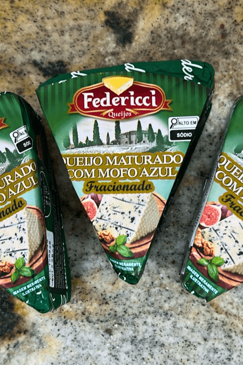 Três peças triangulares de Queijo Maturado com Mofo Azul da marca Federicci, embaladas em papel verde com ilustração de figos e nozes, destacando o rótulo "Alto em Sódio" e o selo de inspeção.