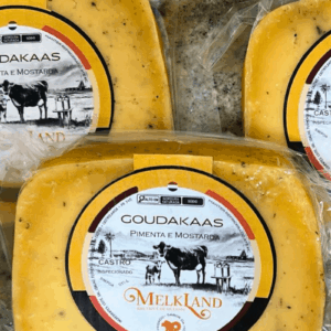 Peças de Queijo Goudakaas com Pimenta e Mostarda da marca Melkland, embaladas a vácuo, mostrando a massa amarela com pontos de especiarias e rótulo circular amarelo e preto.