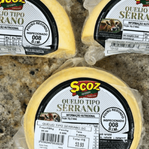 Peças de Queijo Tipo Serrano da marca Scoz, em formato circular e fracionadas, embaladas a vácuo, com rótulo branco e preto destacando o selo de inspeção S.I.M. 008 de Pouso Redondo.