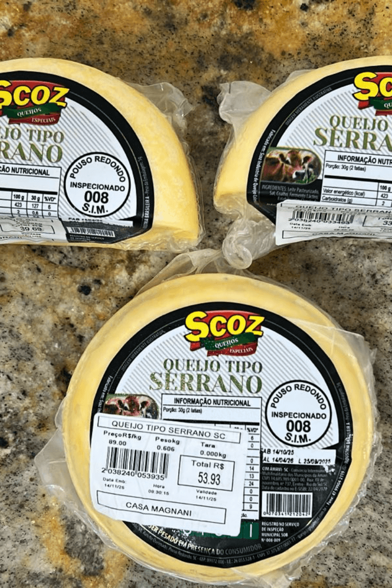 Peças de Queijo Tipo Serrano da marca Scoz, em formato circular e fracionadas, embaladas a vácuo, com rótulo branco e preto destacando o selo de inspeção S.I.M. 008 de Pouso Redondo.